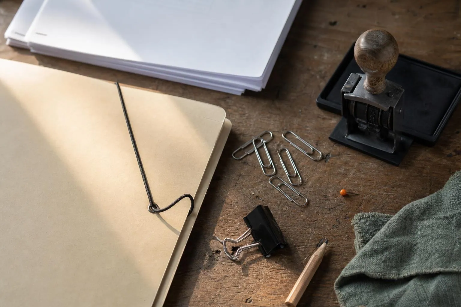 Pochette à élastique, documents empilés, tampon dateur et trombones disposés sur un plan de travail en bois avant classement